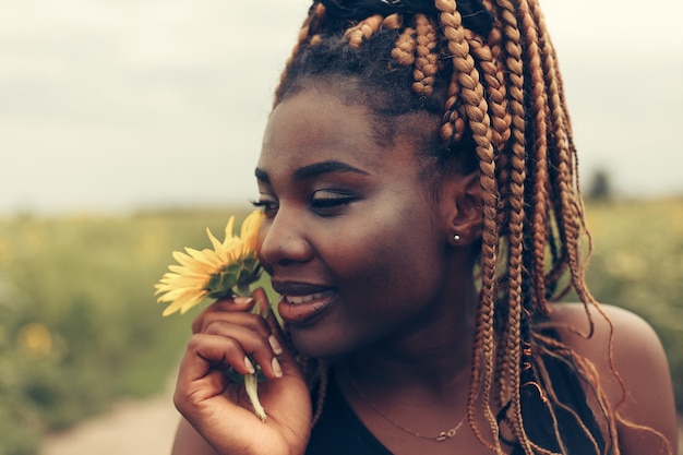 Outdoor portrait of beautiful happy mixed race African American woman in a field of yellow flowers at sunset golden evening sunshine