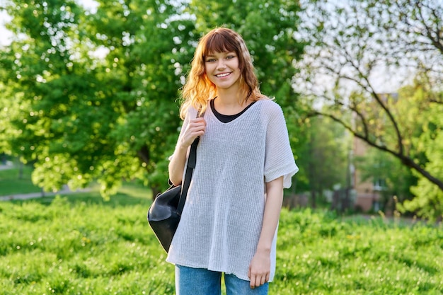 Outdoor portrait of beautiful smiling teen female student with backpack looking at camera