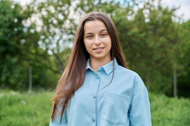 15歳の美しいティーンエイジャーの屋外ポートレート 緑の草の背景に公園でカメラを見ている笑顔の女性ティーンエージャー 青春期 高校時代のコンセプト