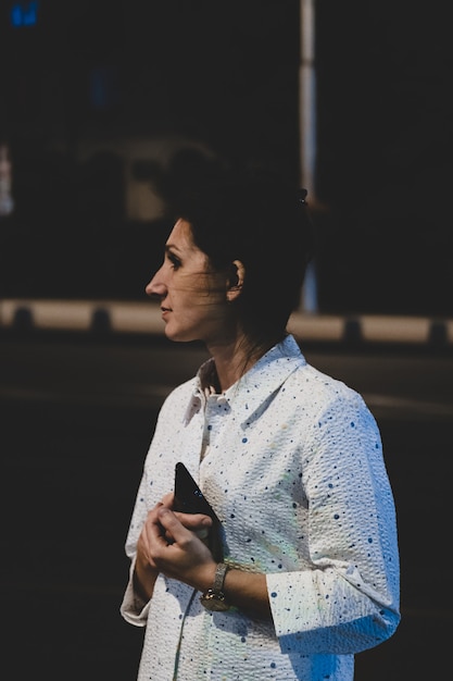 Outdoor portrait of beautiful young woman holding her mobile phone at night. Fashion