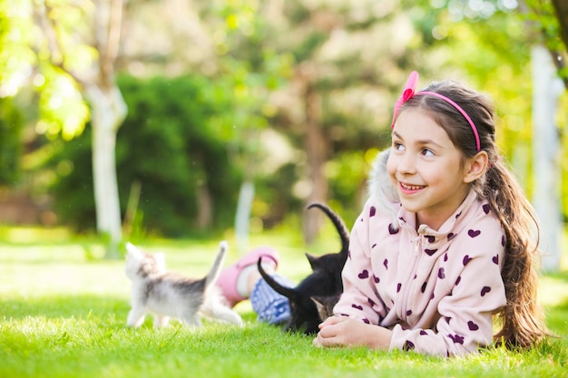 Outdoor portrait of cute girl playing with small kittens on natural background