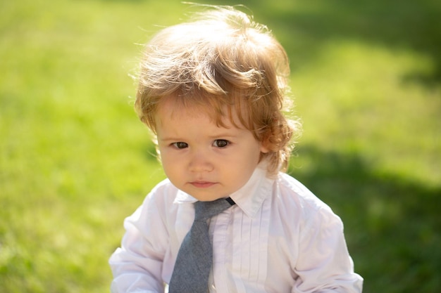 Outdoor portrait of cute little boy in suit and necktie tie little businessman baby child in green g