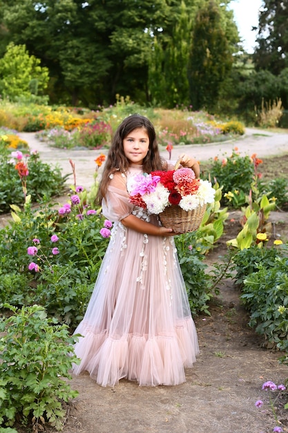 Outdoor portrait of cute little girl holding colorful bouquet of dahlia flowers.  girl holding a basket of peonies
