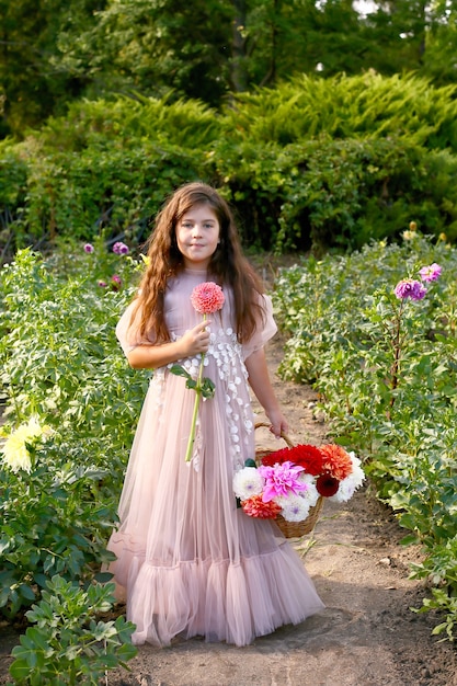 Outdoor portrait of cute little girl holding colorful bouquet of dahlia flowers