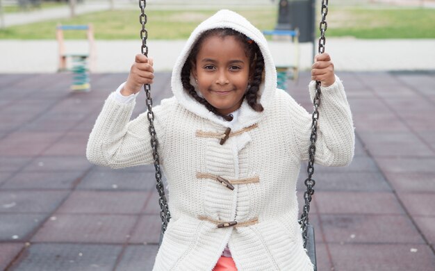 Outdoor portrait of a cute young black girl playing with a swing