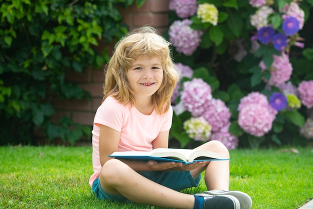 学校の子供たちの教育に戻って本を読んでいるかわいい若い男の子の屋外の肖像画...