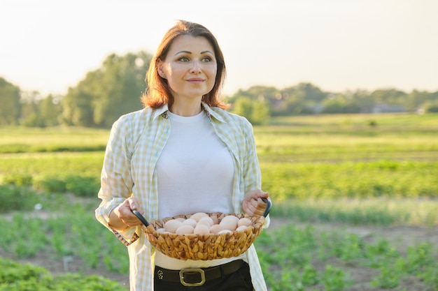 Outdoor portrait of farmer woman with basket of fresh chicken eggs, farm