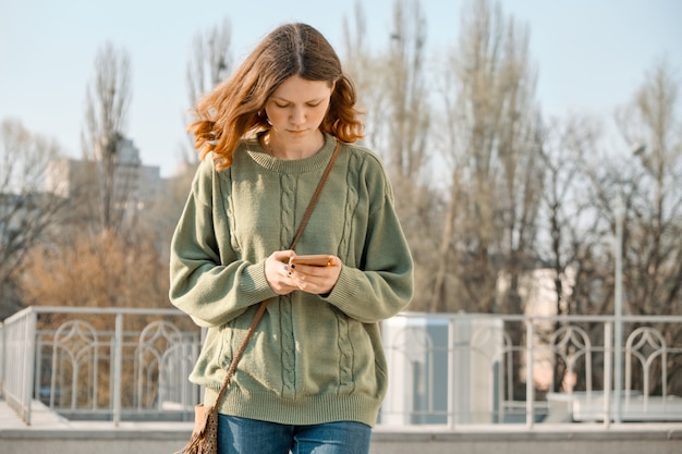 Outdoor portrait of girl walking, reading text message on smartphone