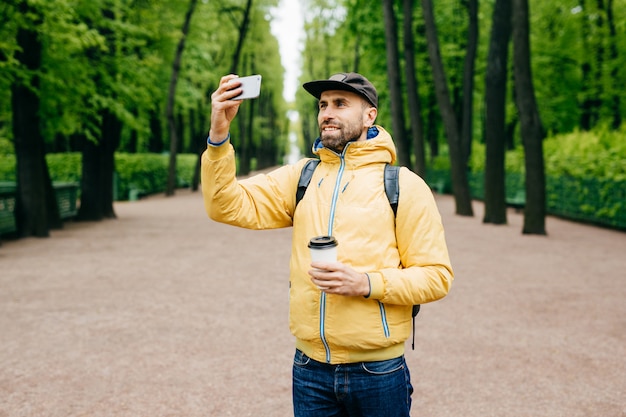 Outdoor portrait of handsome guy with thick beard wearing yellow anorak and jeans holding rucksack