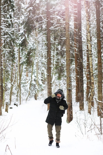 Открытый портрет красивого мужчины в пальто и налетах. Бородатый мужчина в зимнем лесу.