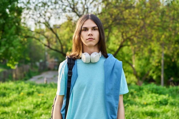 カメラ目線のバックパックを持つハンサムな学生男の屋外のポートレート