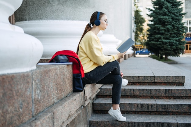 Ritratto all'aperto della giovane donna felice della ragazza dello studente che ascolta le lezioni audio