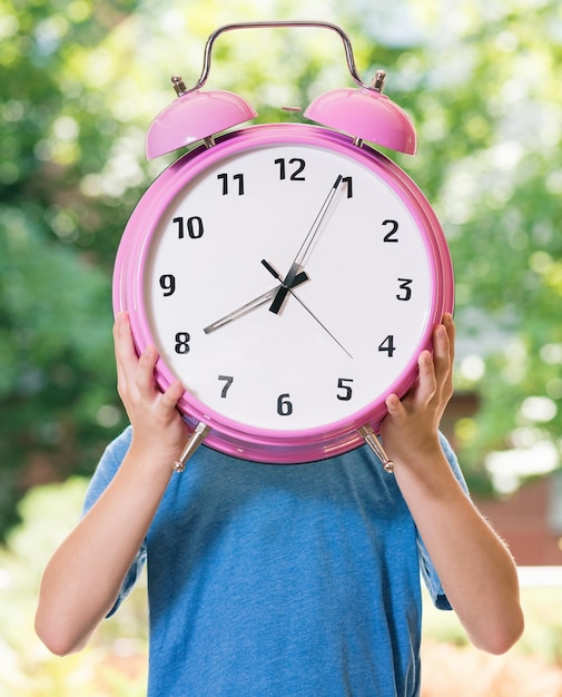 Outdoor portrait of happy teen boy 1214 year old with big alarm clock Back to school concept