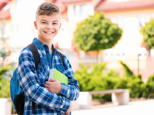 Outdoor portrait of happy teen boy 1214 years old with books and backpack Young student beginning of class after vacation Back to school concept