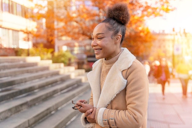 Outdoor portrait of a happy woman holding glasses and smiling in Autumn city