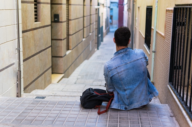 Outdoor portrait of modern young man with smart phone sitting in the street