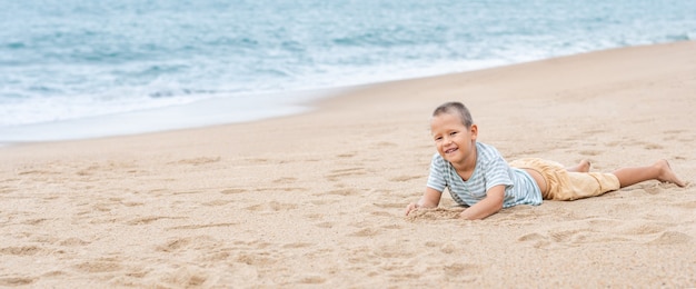 写真 砂浜に横たわっている小さなかわいい男の子の屋外の肖像画。パノラマ