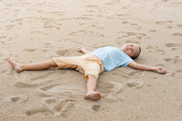 Фото Открытый портрет маленького милого мальчика, лежащего на песчаном пляже.