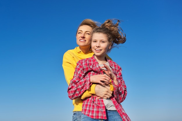 写真 青い空の背景を一緒に抱き締めて幸せな母と子娘の屋外の肖像画