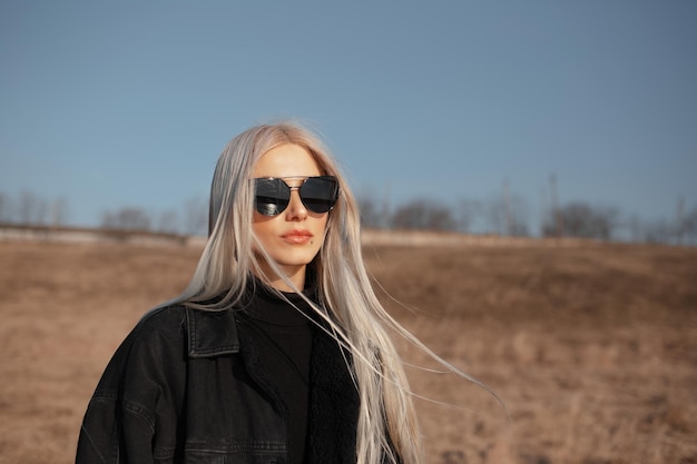 Outdoor portrait of serious cute girl with blonde hair wearing sunglasses