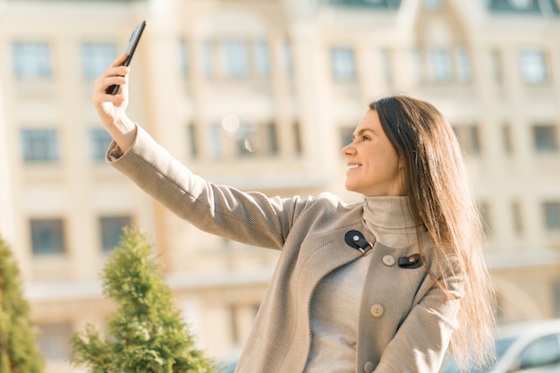 スマートフォンで笑顔の幸せな若い女性の屋外のポートレート