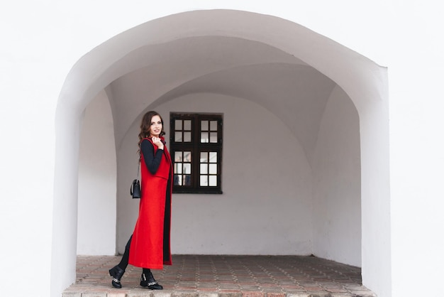 Foto ritratto all'aperto di una ragazza alla moda sulla strada di una città vecchia in abiti neri e un lungo gilet rosso un modello posa sulla strada di una città europea