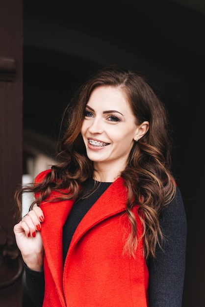 Outdoor portrait of a stylish young girl on the street of an old city in black clothes and a long red vest A model poses on the street of a European city