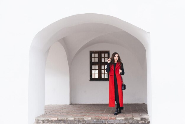 Outdoor portrait of a stylish young girl on the street of an old city in black clothes and a long red vest A model poses on the street of a European city