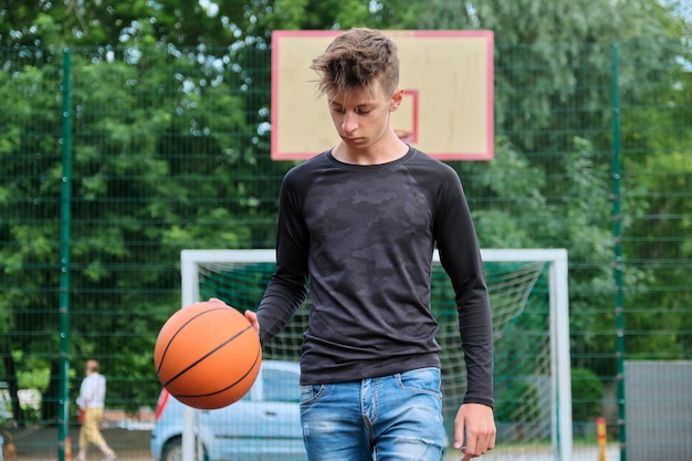 Outdoor portrait of teenage boy playing street basketball, trendy male walking with ball on the court. Active healthy lifestyle, hobbies and leisure, teenagers concept