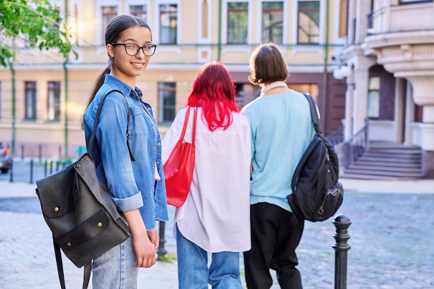 アウトドアポートレート ティーンエイジャーの女性学生 街で街で 笑顔の女性ティーンエイト 眼鏡をかぶったバックパックで カメラを見ている 背中を背負った若い人々を歩いている