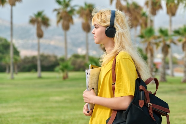 Outdoor portrait of teenage female student in headphones with laptop backpack