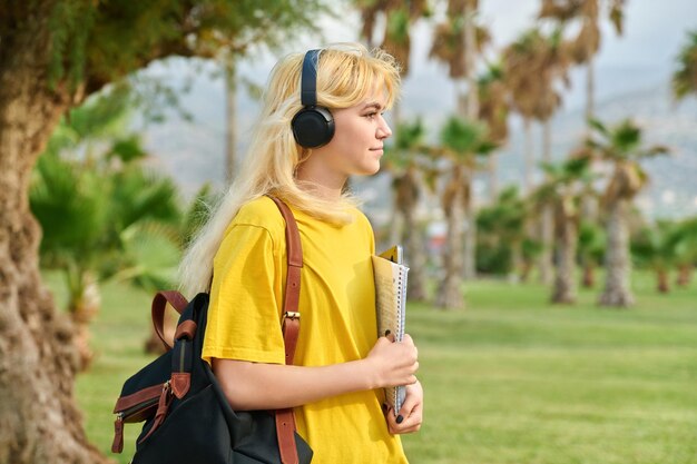 Outdoor portrait of teenage female student in headphones with laptop backpack