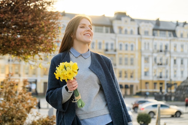 Outdoor portrait of young beautiful girl with bouquet of yellow spring flowers