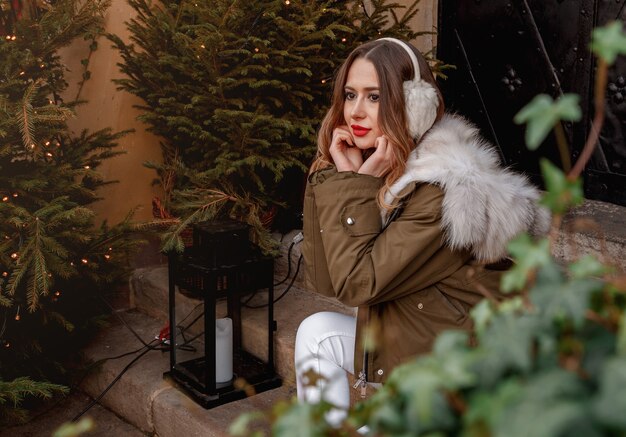 Outdoor portrait of young beautiful happy smiling girl is wearing fur coat near decorated Christmas tree