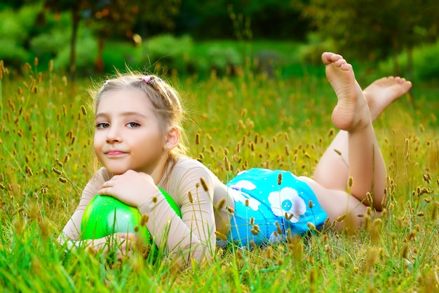 Outdoor portrait of young cute little girl gymnast training with ball on grass