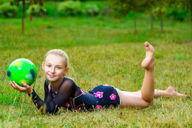 Outdoor portrait of young cute little girl gymnast training with ball on grass