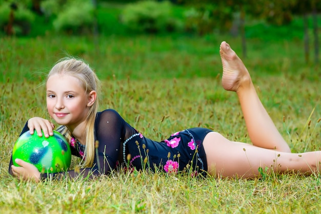 Outdoor portrait of young cute little girl gymnast training with ball on grass