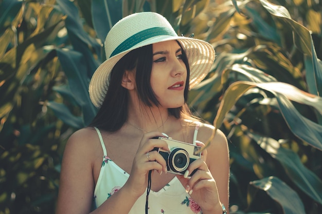 Outdoor portrait of a young hispanic girl wearing summer dress and hat taking photos