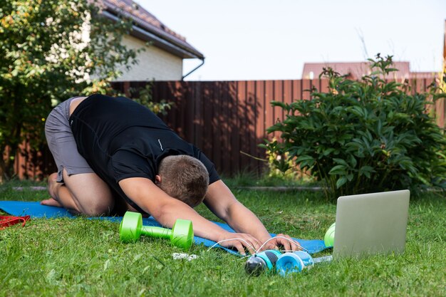 Outdoor portrait of the young man in a sports uniform is resting, stretching on the lawn  in garden