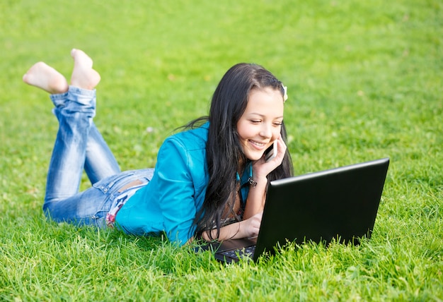 Outdoor portrait of young woman lying down using a laptop