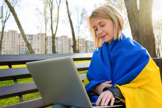 Открытый портрет молодой женщины с украинским флагом, работающей по видеосвязи на компьютере в парке