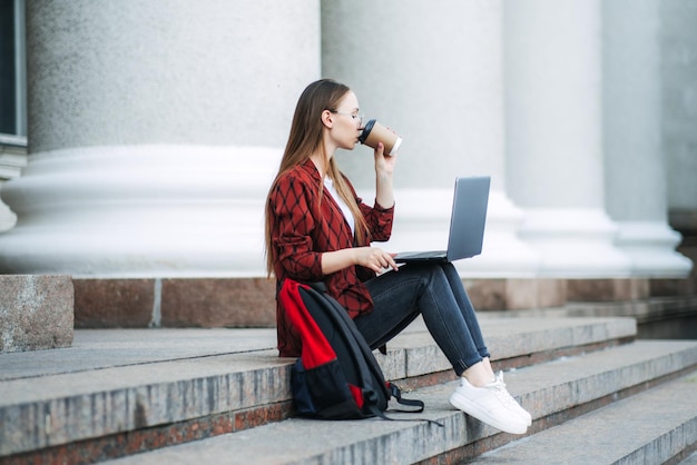 Outdoor portret van vrouwelijke student met koffiekopje en laptop studente heeft koffiepauze after