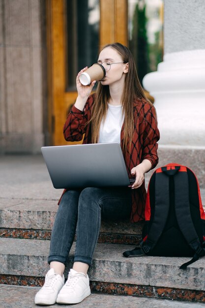 Outdoor portret van vrouwelijke student met koffiekopje en laptop studente heeft koffiepauze after