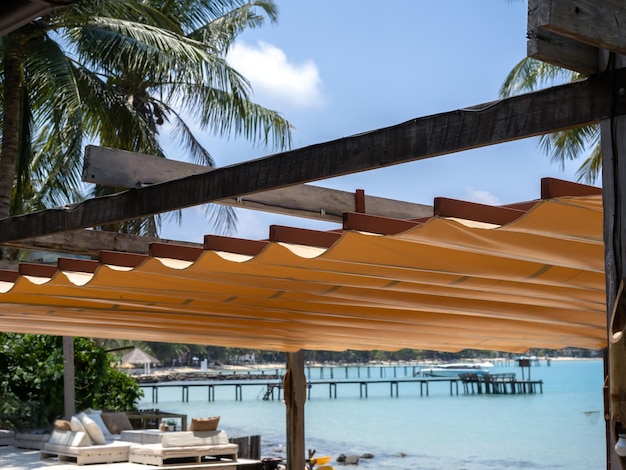 Outdoor retractable roof on wood and iron construction on the beach front restaurant near the tropical palm tree and seascape view background Foldable fabric canvas awning on the seaside