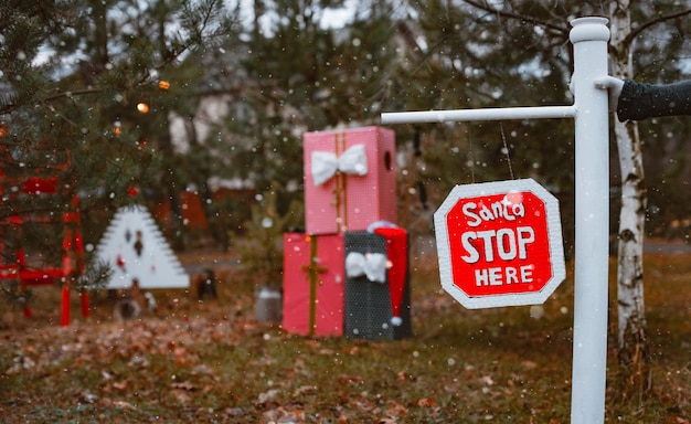 Открытый дорожный барьер в рождественских украшениях на соснах с надписью Санта, пожалуйста, остановитесь здесь