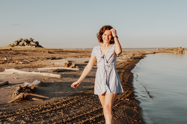 Outdoor sfeervolle levensstijl foto van jonge mooie donkerharige vrouw in zomerjurk wandelen op het strand.