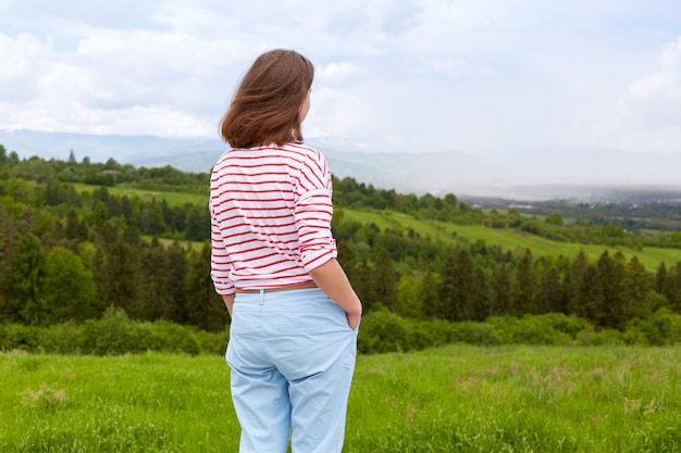 Outdoor shot of attractive young woman wearing casual trousers and white t shirt with red stripes