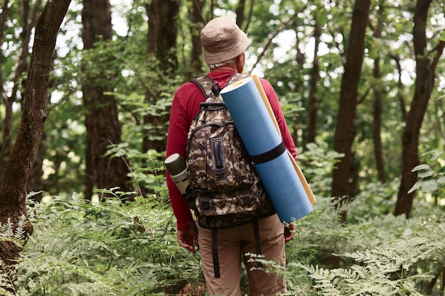 Outdoor shot of elderly man travels to top of mountain, old man tourist in mountains carries rucksack and rug