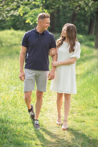 Outdoor shot of young couple in love walking on road through grass field man and woman are happy tog