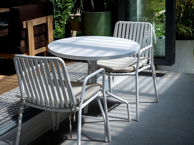 Outdoor small table set at the restaurant or cafe Two empty chairs with pads and empty white round table in front of the coffee shop